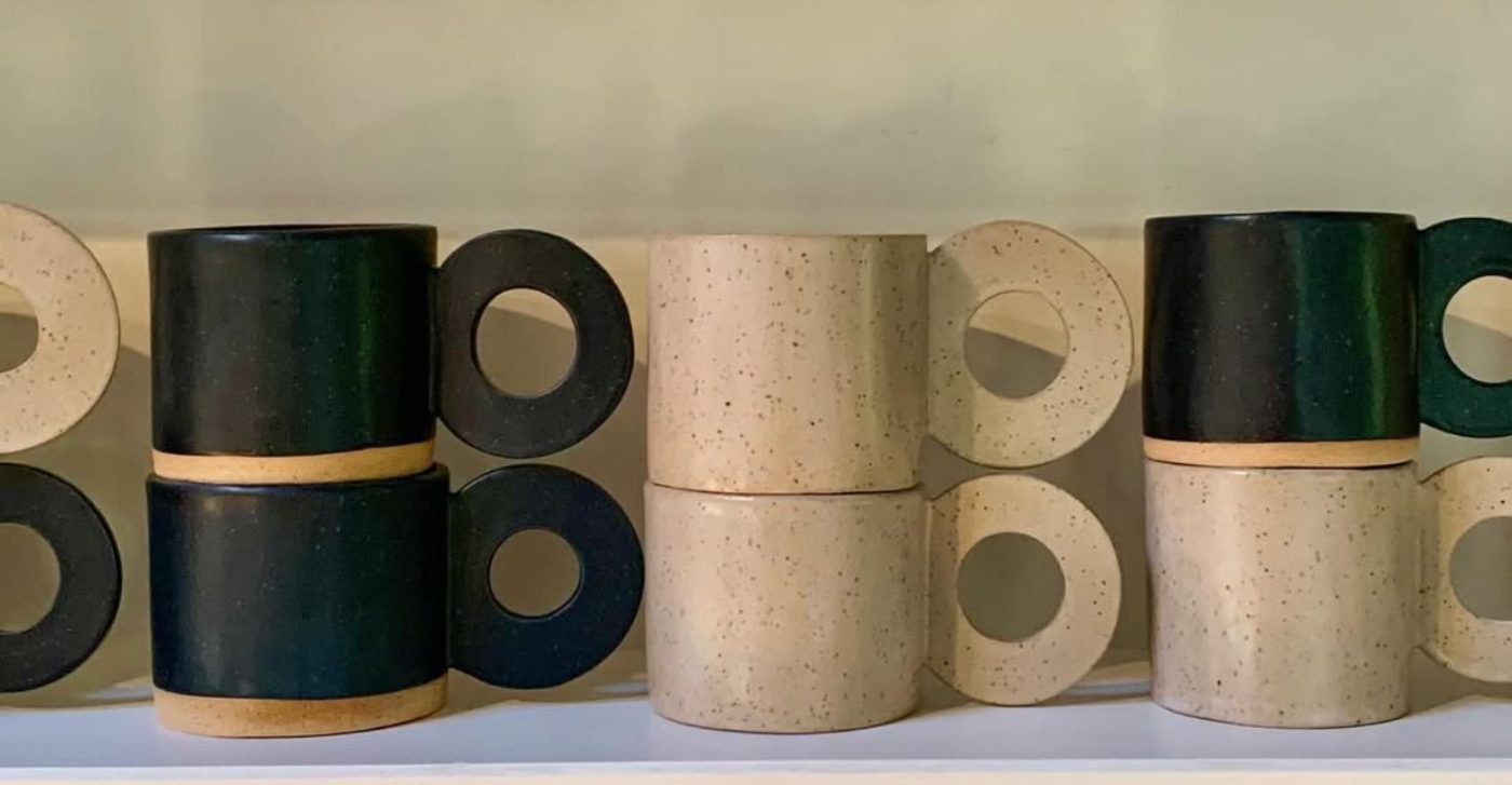 Stacked circle-handle mugs in dark green and speckled cream